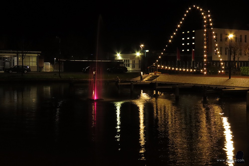 gekleurde fontein in de passentenhaven aan het Moleneind. Op de achtergrond branden de lichtjes van het skûtsje 'de Jonge Trijntje'