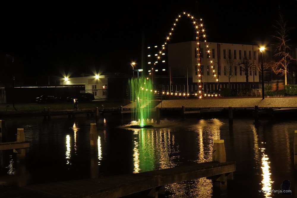 gekleurde fontein in de passentenhaven aan het Moleneind. Op de achtergrond branden de lichtjes van het skûtsje 'de Jonge Trijntje'
