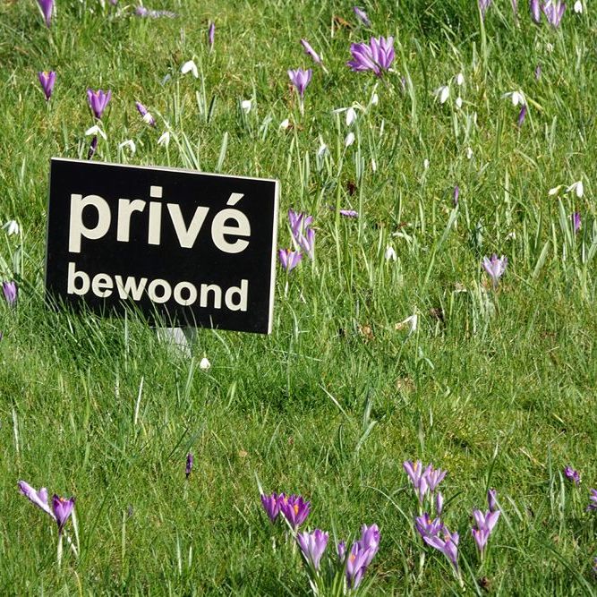 bordje 'prive'- bewoond' staat in het gras tussen bloeiende krokussen